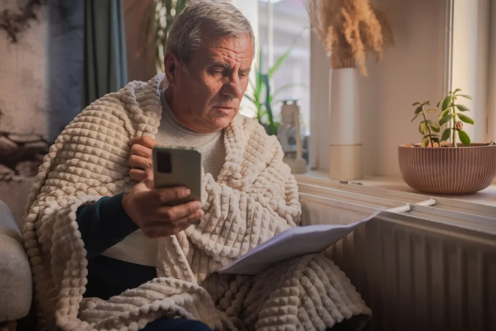 Senior staying warm indoors with a blanket and hot drink during cold weather