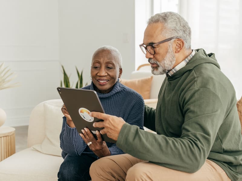 senior couple sitting on their couch looking at their tablet