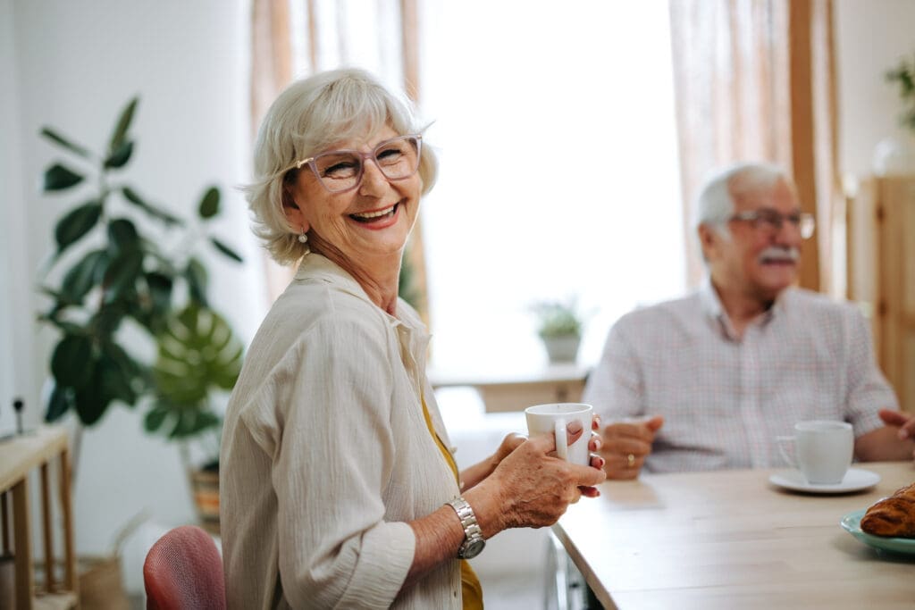 Senior woman at a table with friends holding mug and smiling